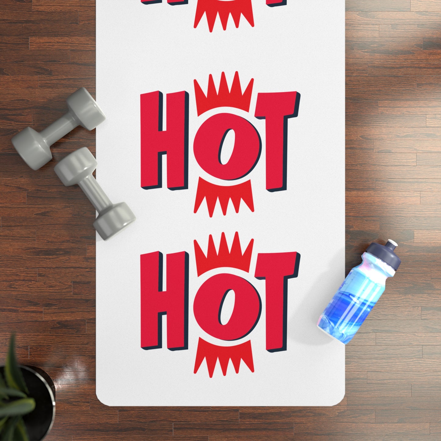 Yoga mat with 'HOT' text on a wooden floor with dumbbells and a water bottle.