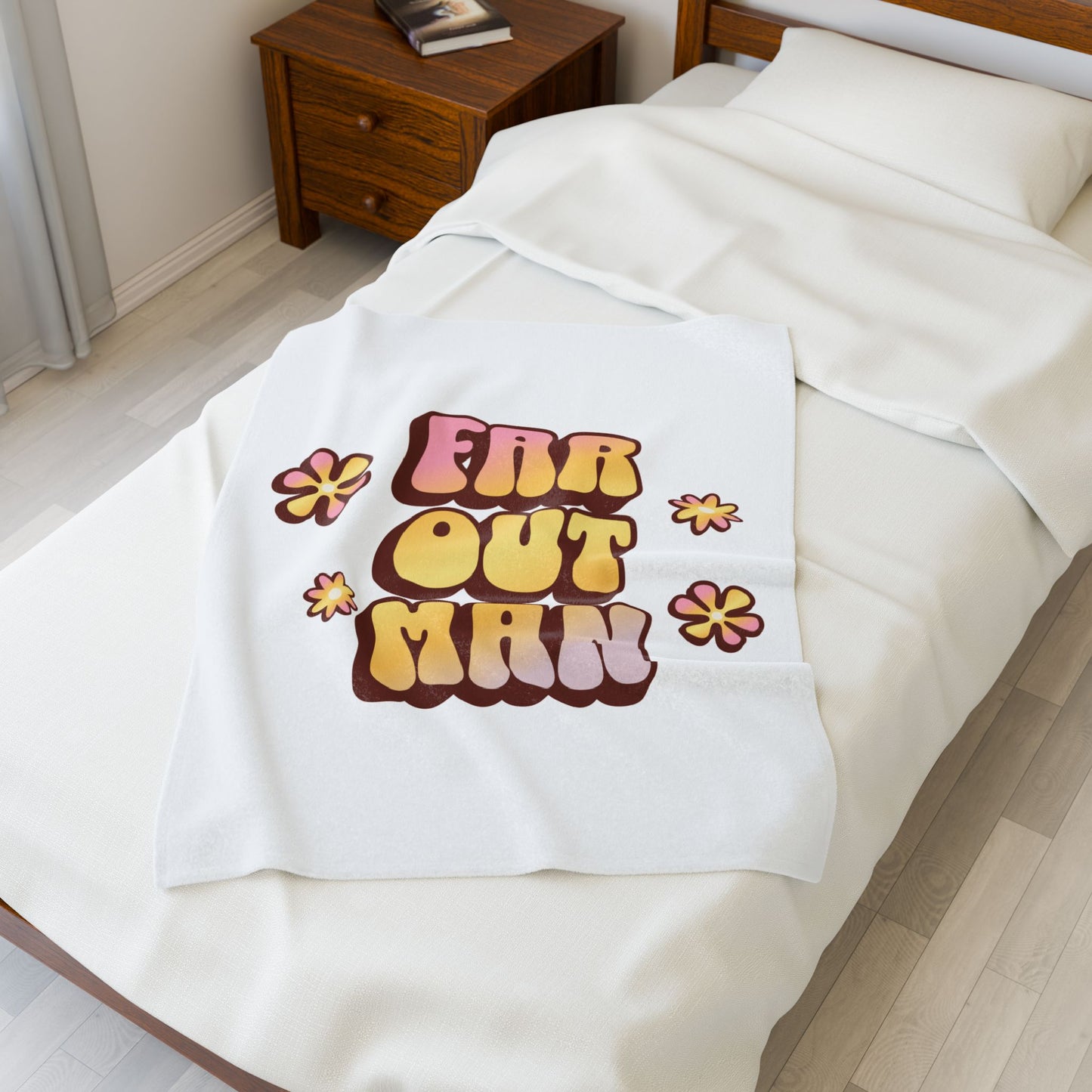 White blanket with 'Far Out Man' text and flowers on a bed in a bedroom.