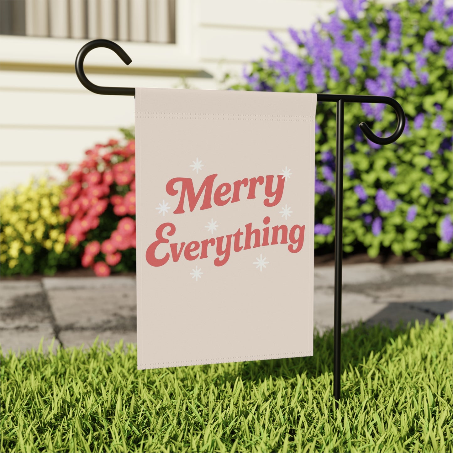 Garden flag with 'Merry Everything' text on a stand in front of flowers