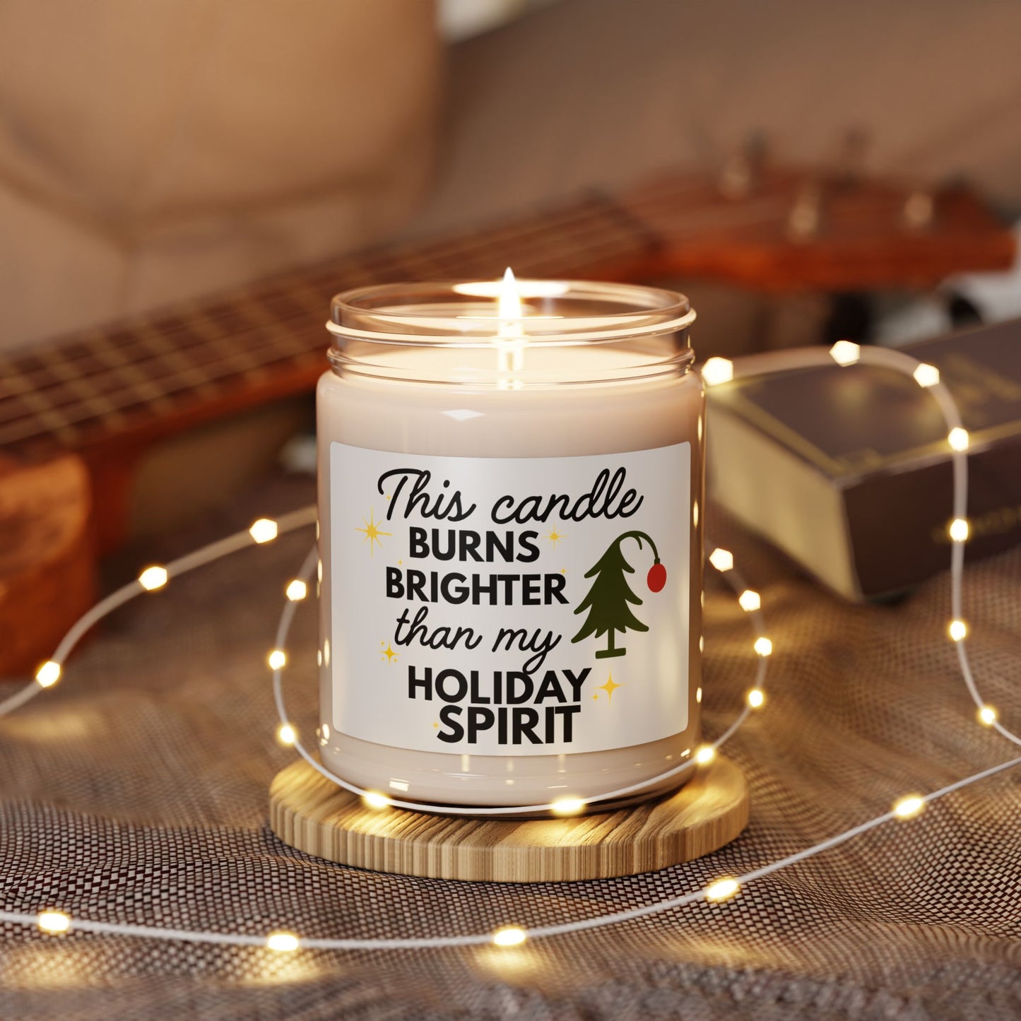 Candle with a decorative label on a wooden coaster surrounded by string lights and a guitar in the background