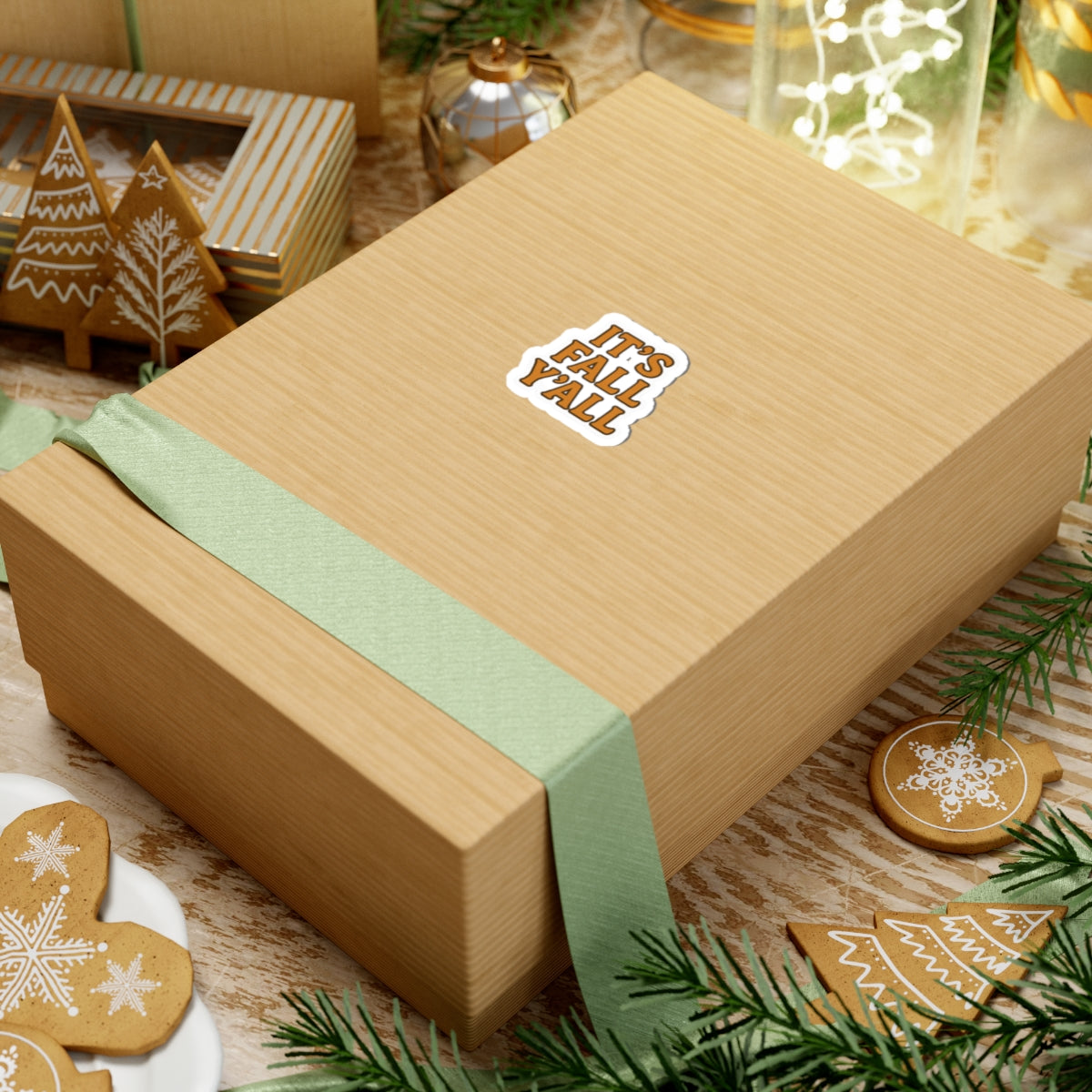 Wooden gift box with a green ribbon and 'It's Fall Y'all' sticker, surrounded by Christmas decorations.