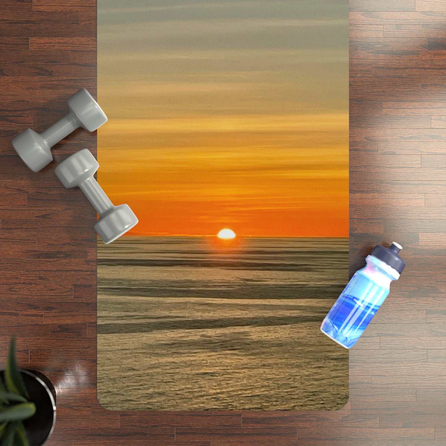 Yoga mat with sunset design, dumbbells, and water bottle on a wooden floor.