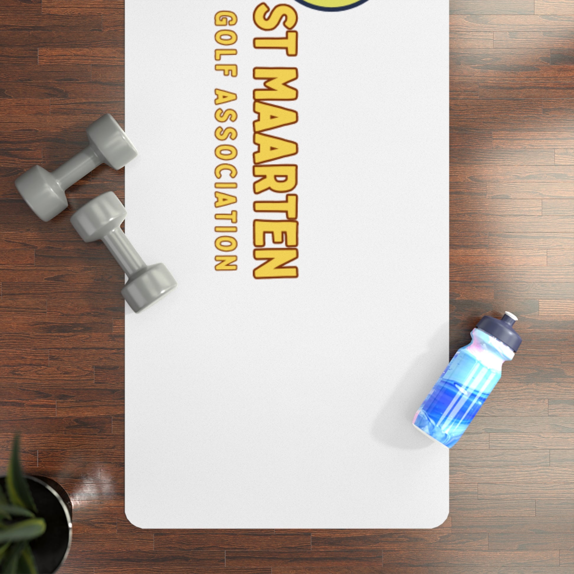 White mat with 'St Maarten Golf Association' text, dumbbells, and a water bottle on a wooden floor.