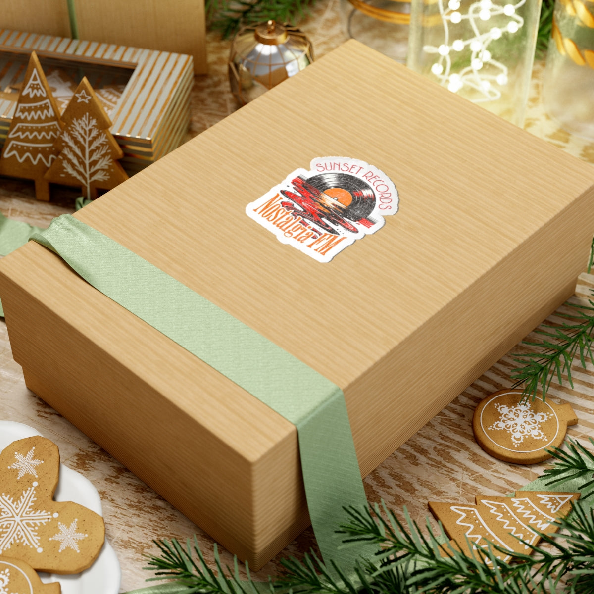 Gift box with a green ribbon and decorative sticker on a festive background with cookies and lights.