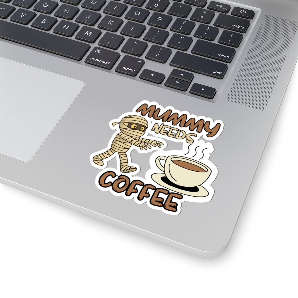 Laptop with a sticker of a mummy needing coffee on the palm rest area.