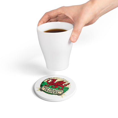 Hand holding a white mug with a Red Dragon Traders coaster underneath on a white background