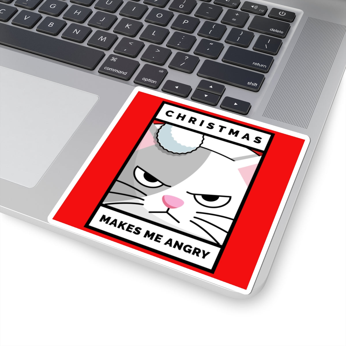 Laptop with a sticker of a cat's face and text 'Christmas makes me angry' on a red background.