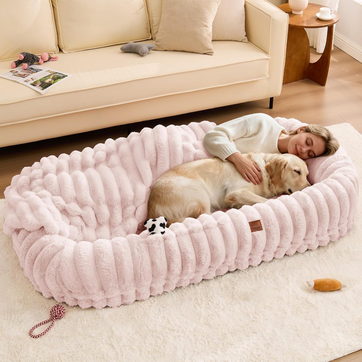 Woman lying on a pink pet bed with a dog in a living room setting.