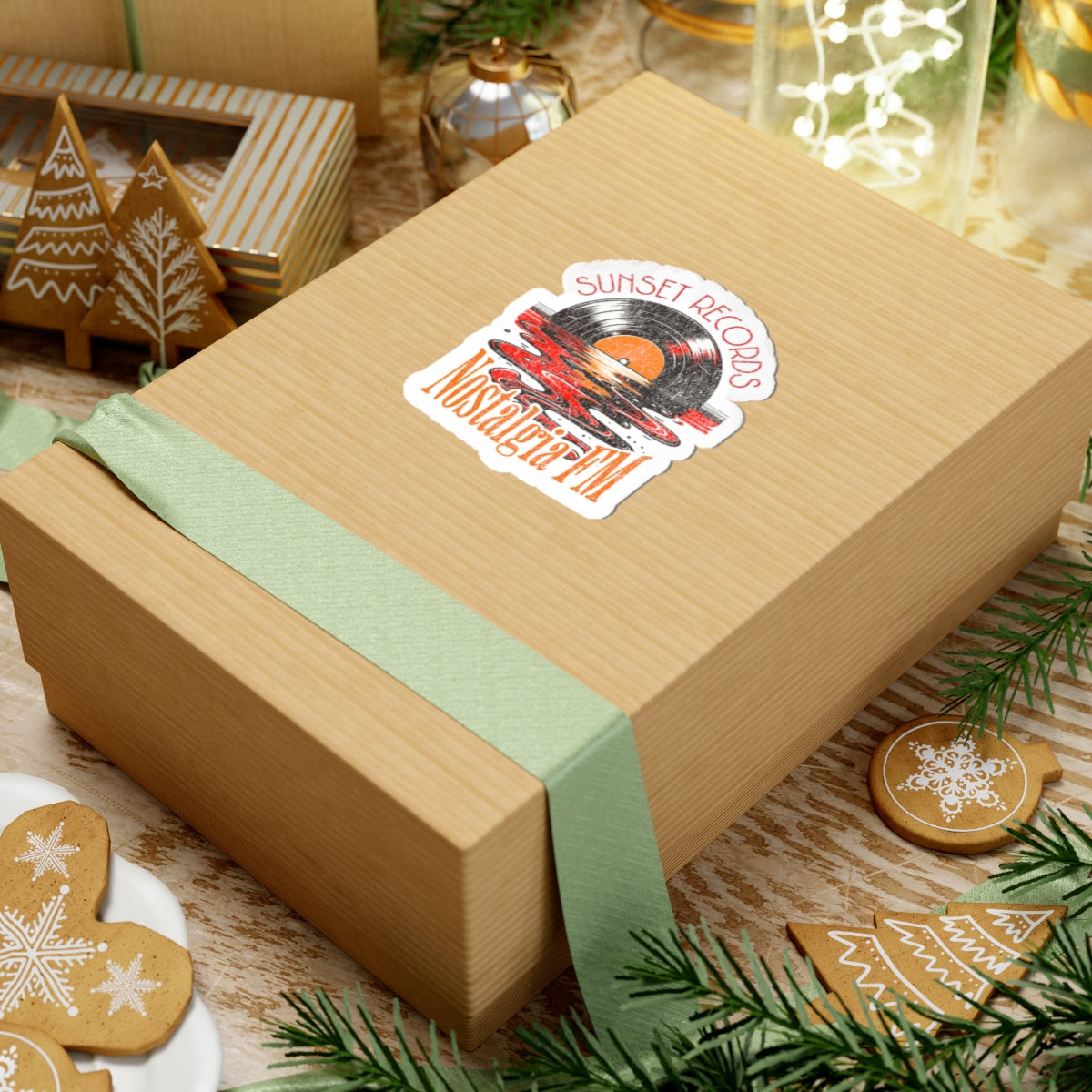 Wooden gift box with a green ribbon and a decorative sticker on a festive background with cookies and lights.