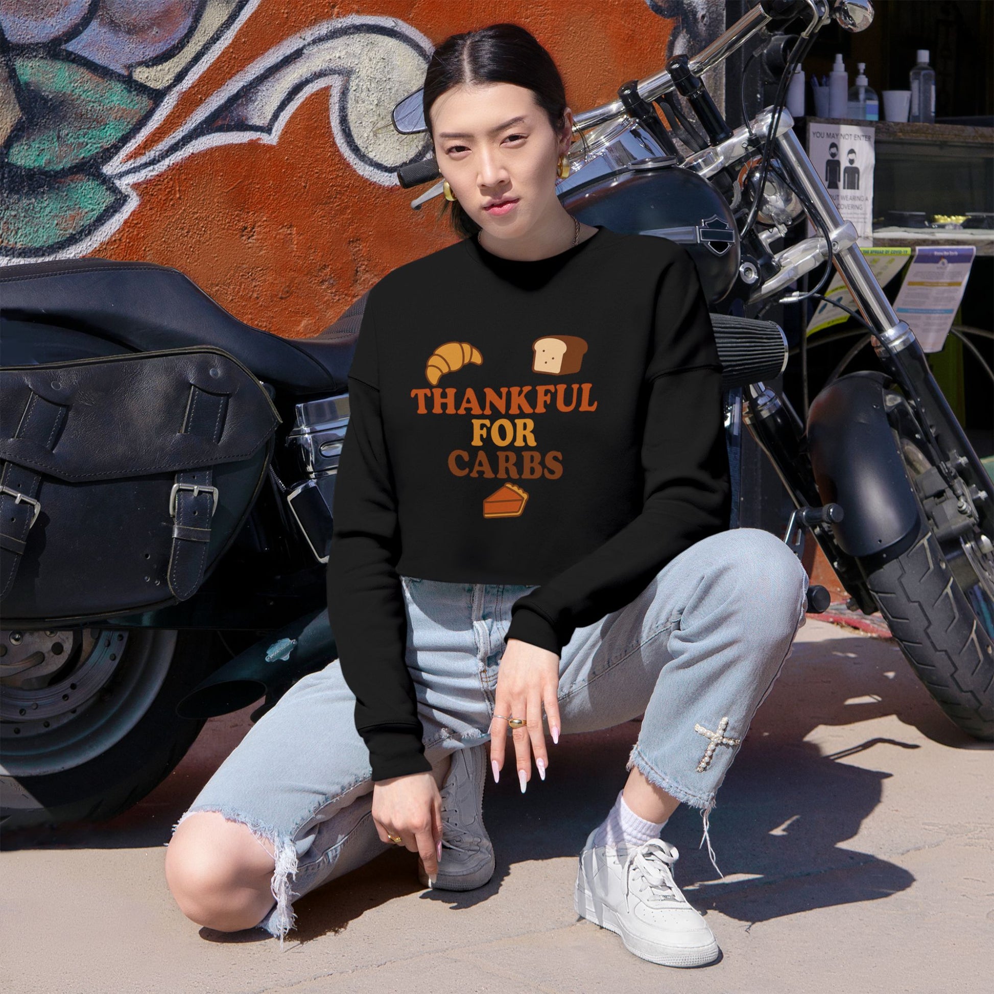 Person wearing a black sweatshirt with text, sitting next to a motorcycle.