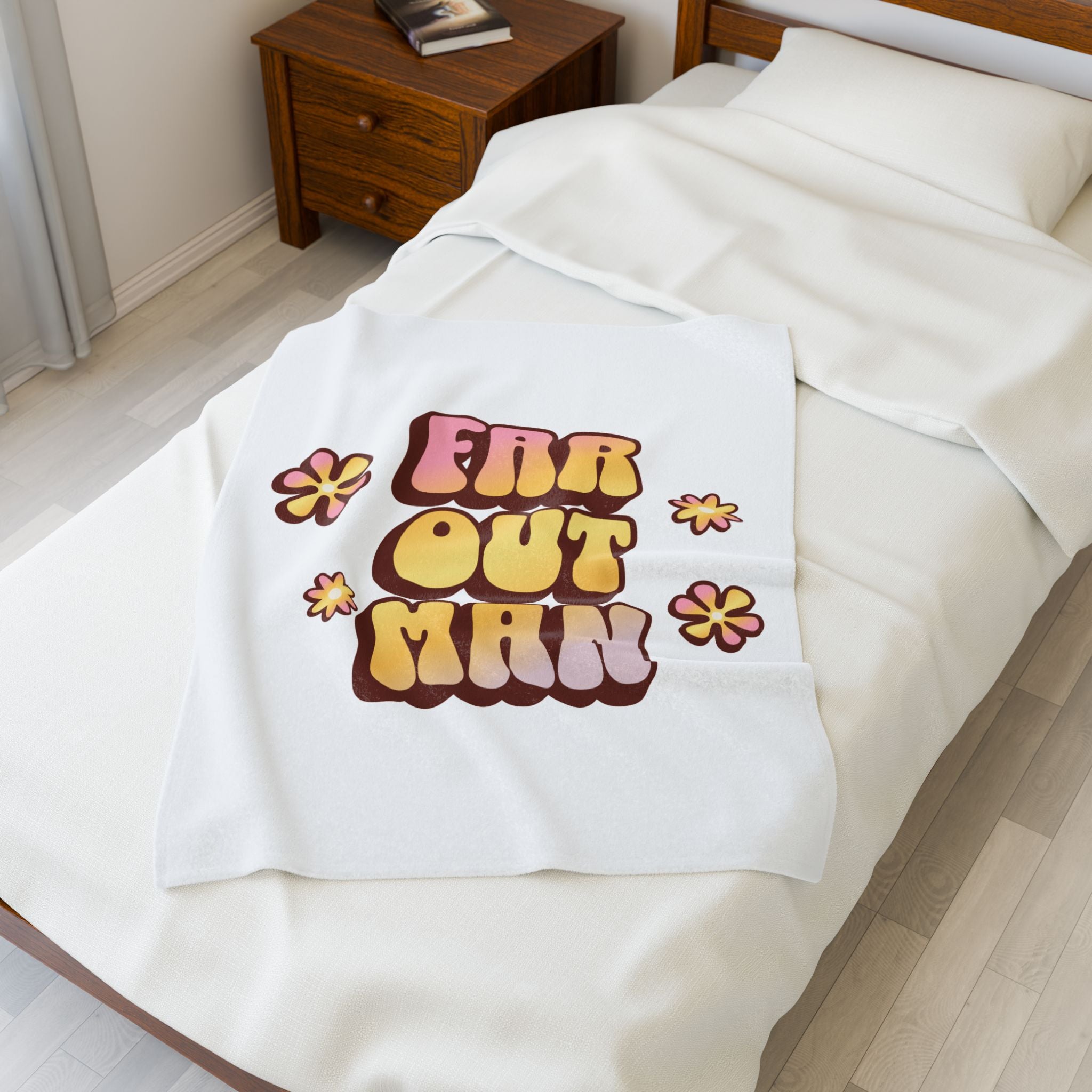 White blanket with 'Far Out Man' text and flowers on a bed in a bedroom.