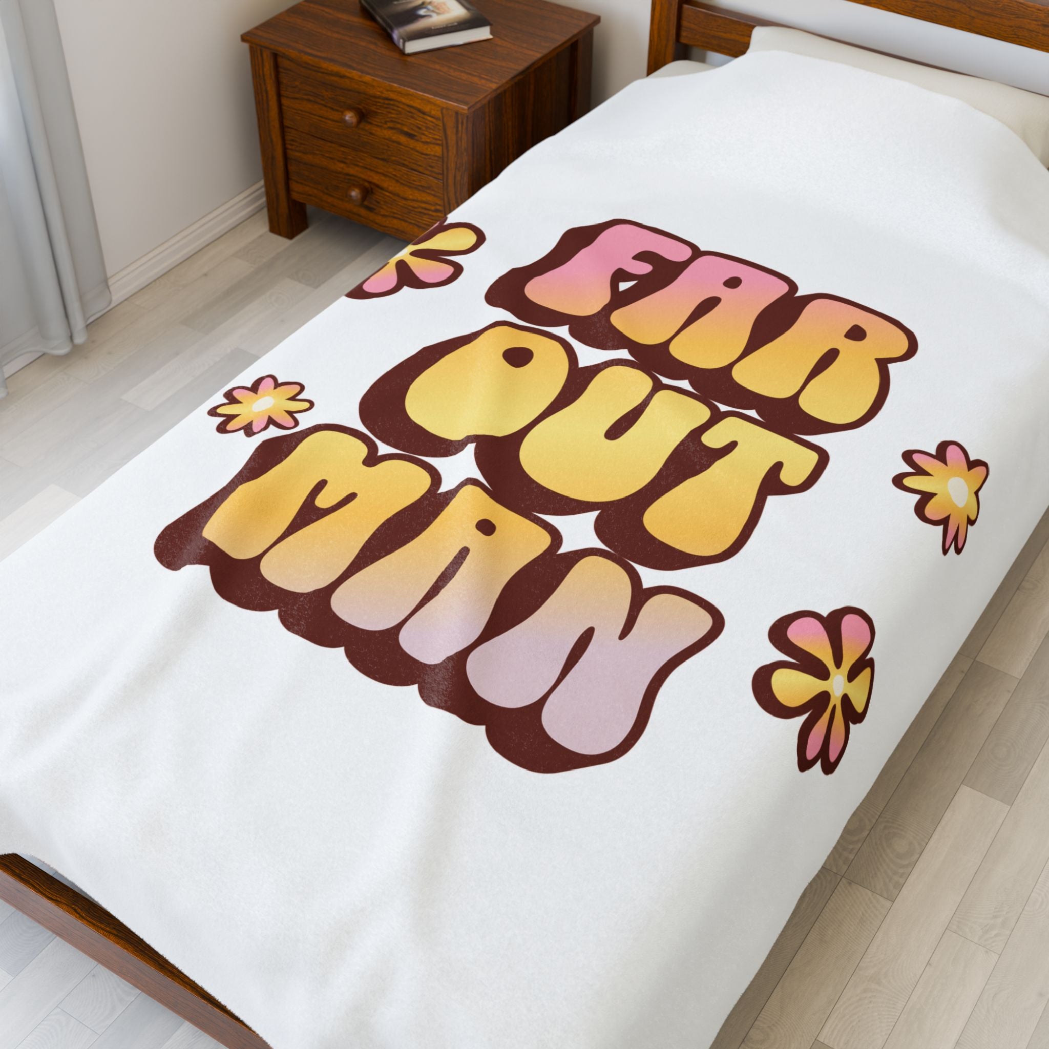 Blanket with 'Far Out Man' text and flowers on a bed in a room.