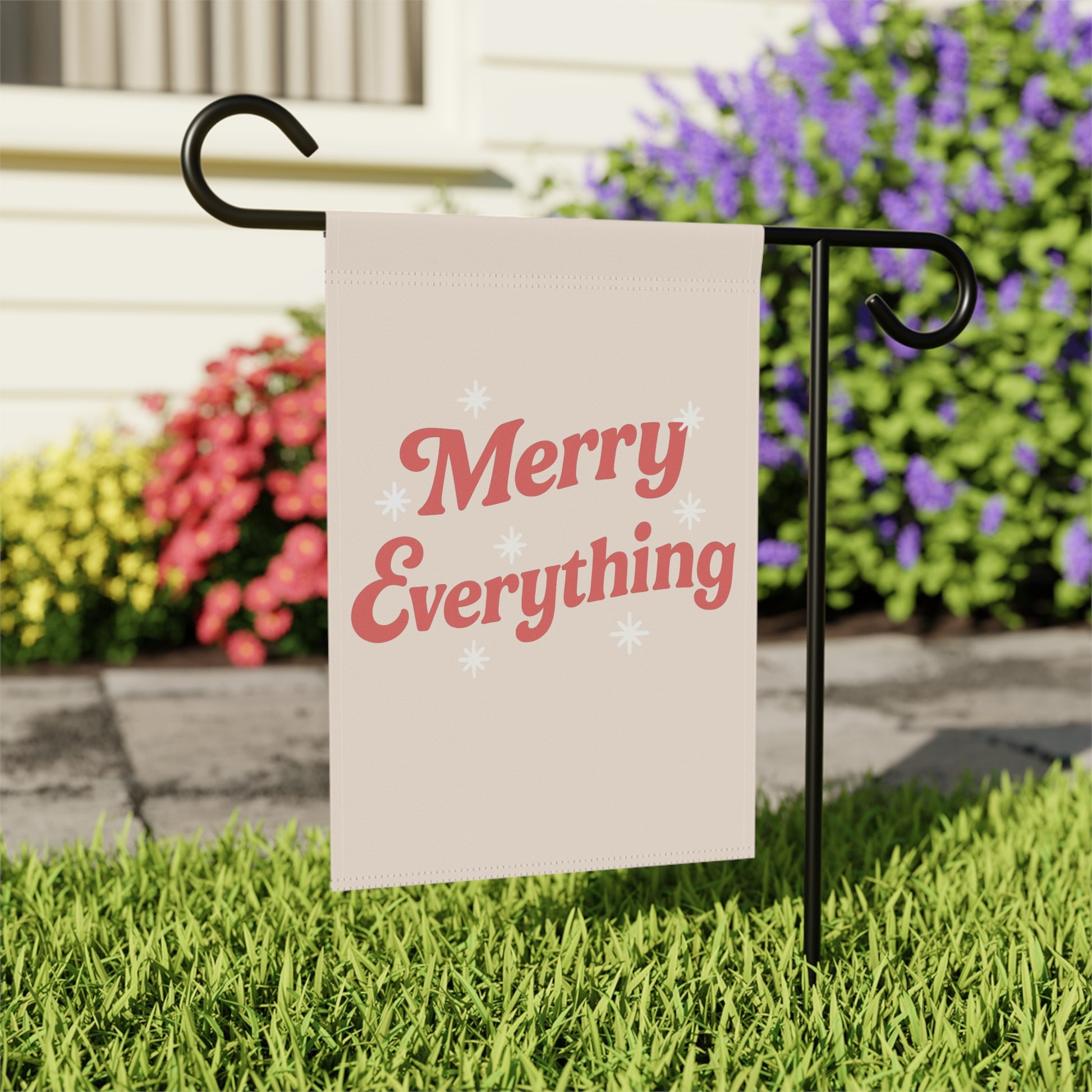 Garden flag with 'Merry Everything' text on a stand in front of flowers