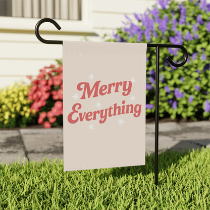 Garden flag with 'Merry Everything' text on a stand in front of flowers