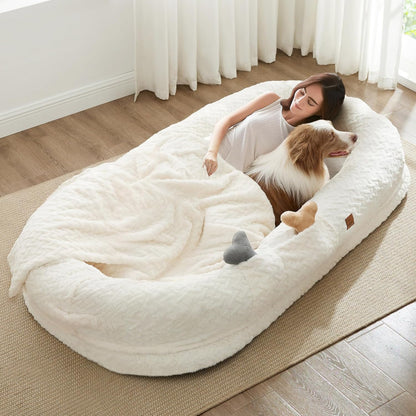 Person lying on a large white pet bed with a dog inside, in a bright room with curtains.
