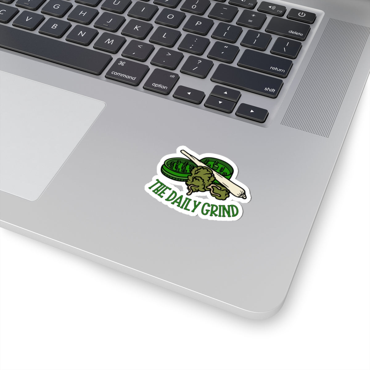 Laptop with a 'The Daily Grind' sticker featuring a green grinder and rolling pin.