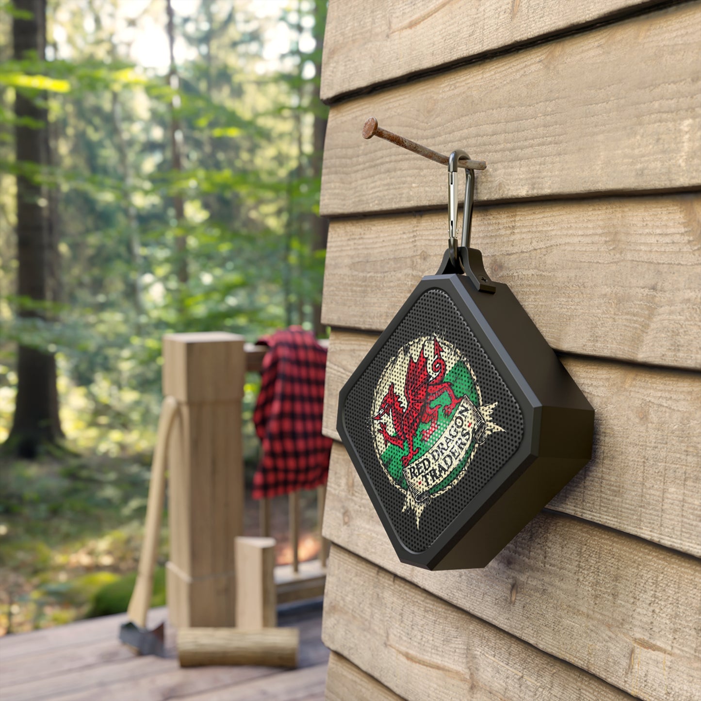 Black Bluetooth speaker with a dragon design hanging on a wooden wall outdoors.