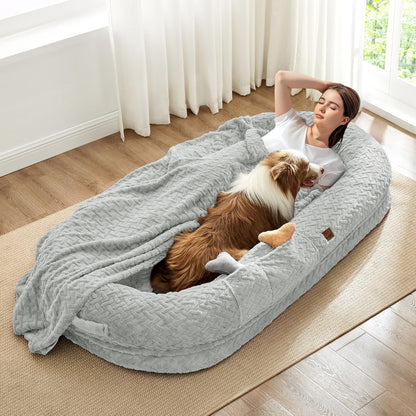 Woman lying on a large gray pet bed with a dog, in a bright room with curtains.